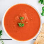 overhead view of Instant Pot tomato soup, garlic clove, toasted bread, and parsley