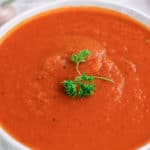 closeup photo of a bowl of Instant Pot tomato soup and a sprig if fresh parsley