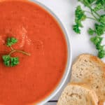 overhead view of a bowl of tomato soup, toasted bread slices, and fresh parsley
