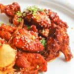 spicy chicken wings with sauce, sesame seeds, and green onions on a plate