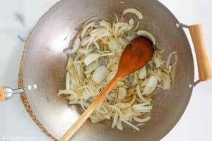 sliced onions and a wooden spoon in a wok