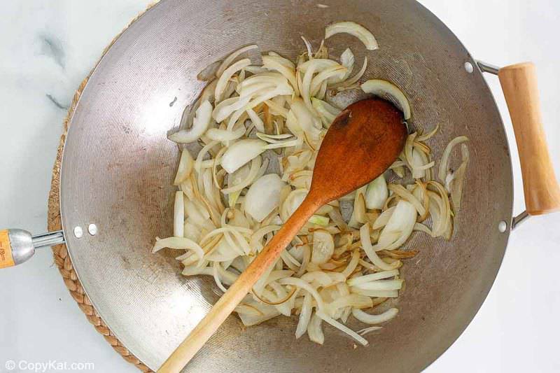 cebollas en rodajas y una cuchara de madera en un wok