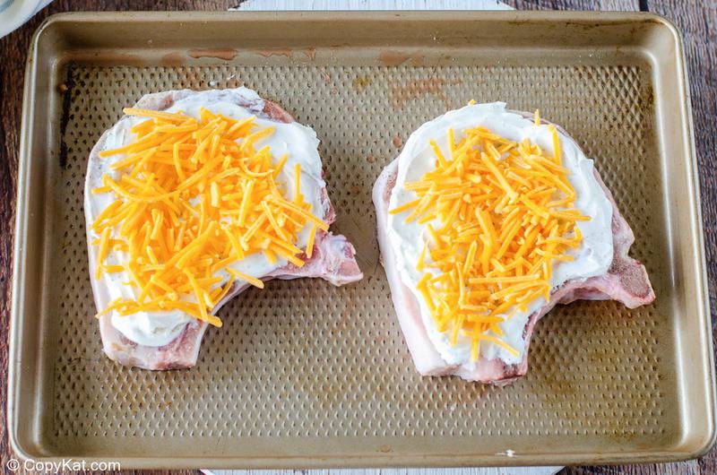 pork chops topped with sour cream and shredded cheese on a baking sheet
