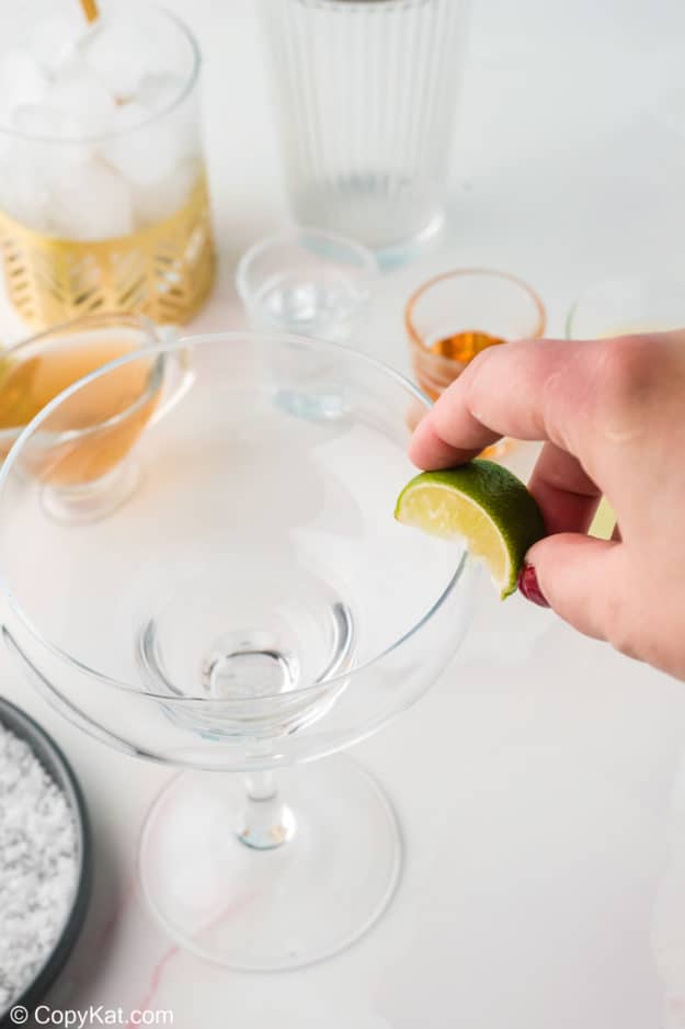 rubbing a lime wedge on the rim of a margarita glass
