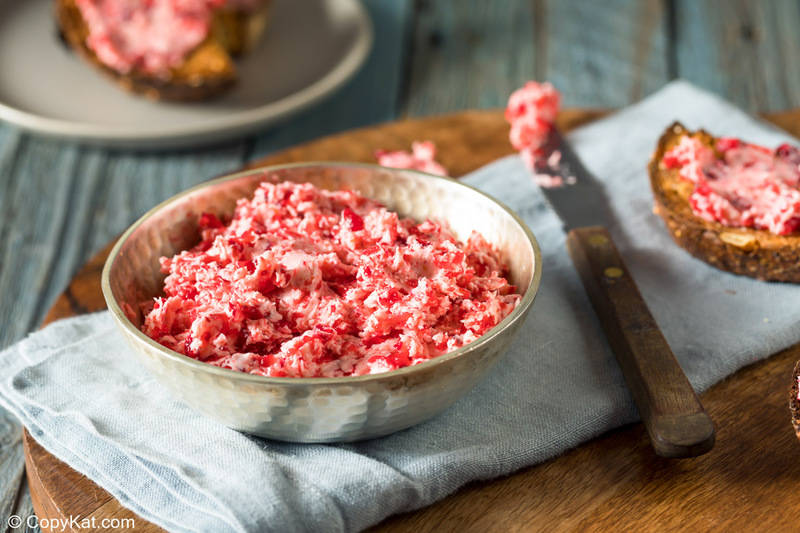 cranberry butter in a bowl, a knife, and bread slices with the butter on them.