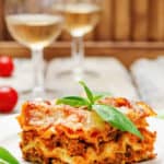 homemade lasagna on a plate and two glasses of white wine