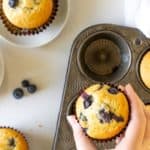 hand picking up a blueberry muffin out of a muffin tin