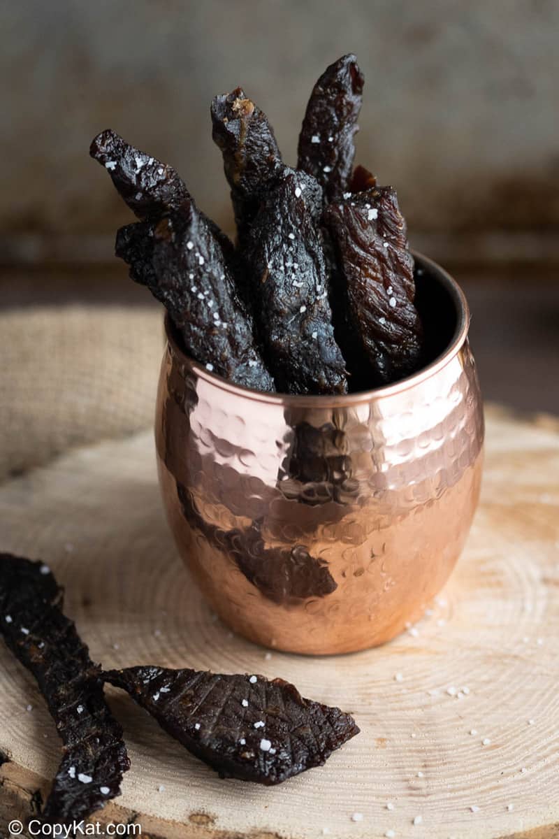 homemade teriyaki beef jerky strips in a cup and on a wood board
