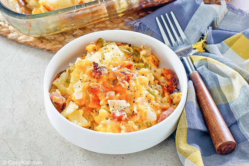 a bowl of cheesy scalloped potatoes and ham casserole next to a fork and napkin
