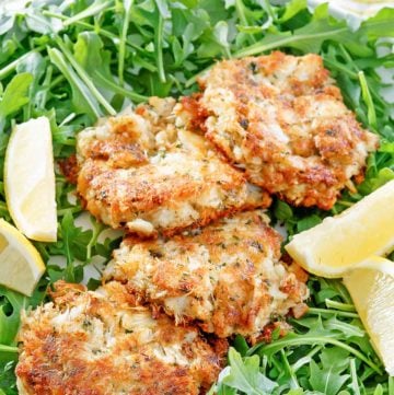 four Maryland crab cakes, lemon wedges, and arugula on a platter