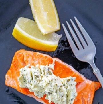 overhead view of salmon with pesto cream cheese sauce and two lemon wedges on a plate