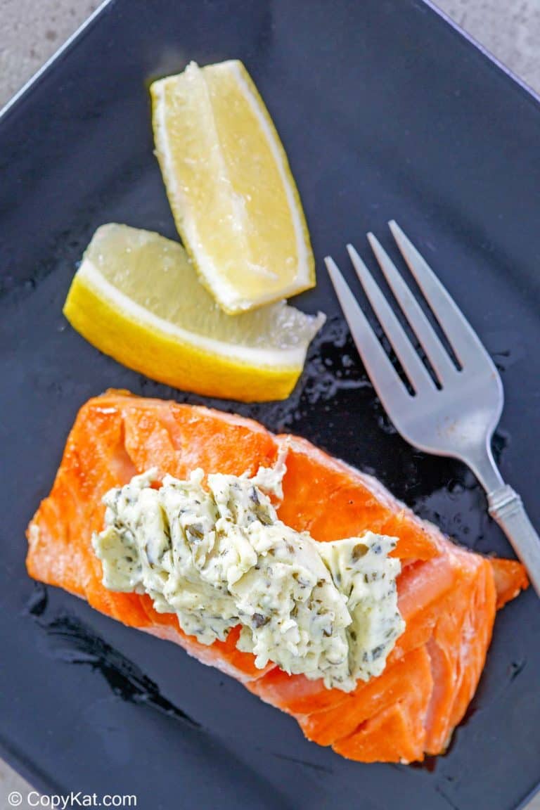 overhead view of salmon with pesto cream cheese sauce and two lemon wedges on a plate