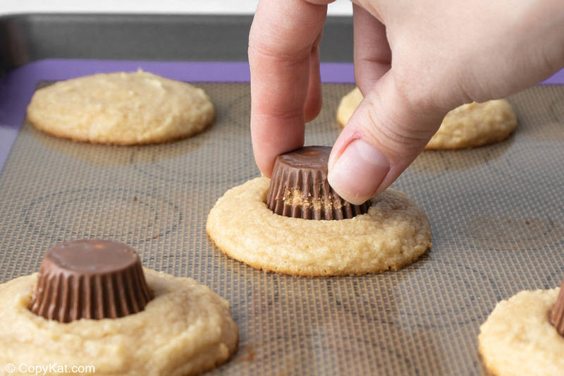 pressing a mini peanut butter cup into a freshly baked cookie