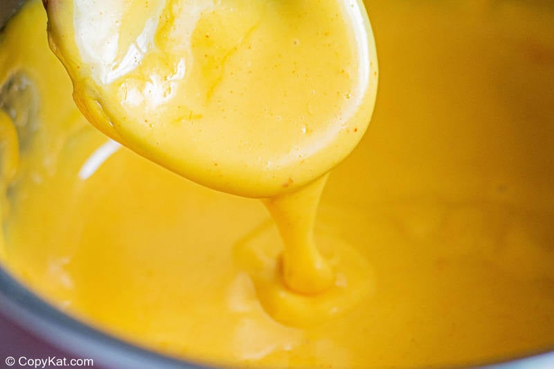 nacho cheese sauce pouring from a wooden spoon into a pot
