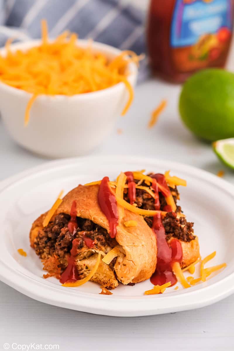 piece of a taco ring on a plate and a bowl of shredded cheese