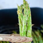 tongs holding three spears of air fried asparagus