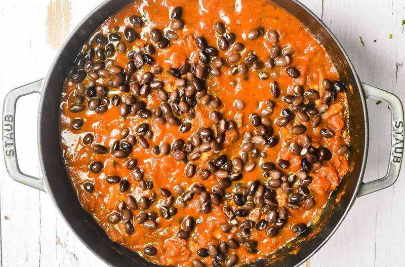 adding black beans to tomato sauce for huevos rancheros