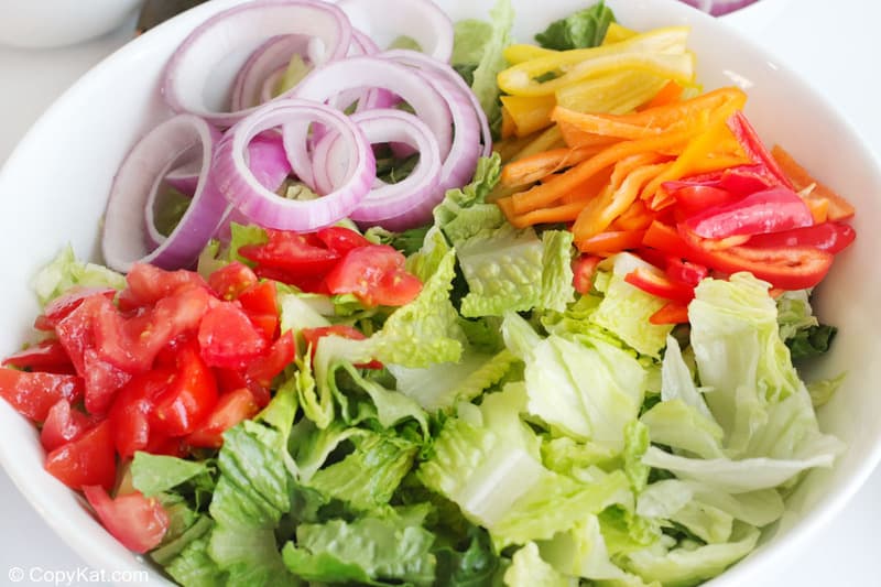 romaine lettuce, chopped tomatoes, red onion slices, and bell pepper slices in a bowl