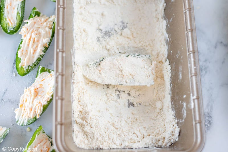 coating a cheese stuffed jalapeno pepper in flour