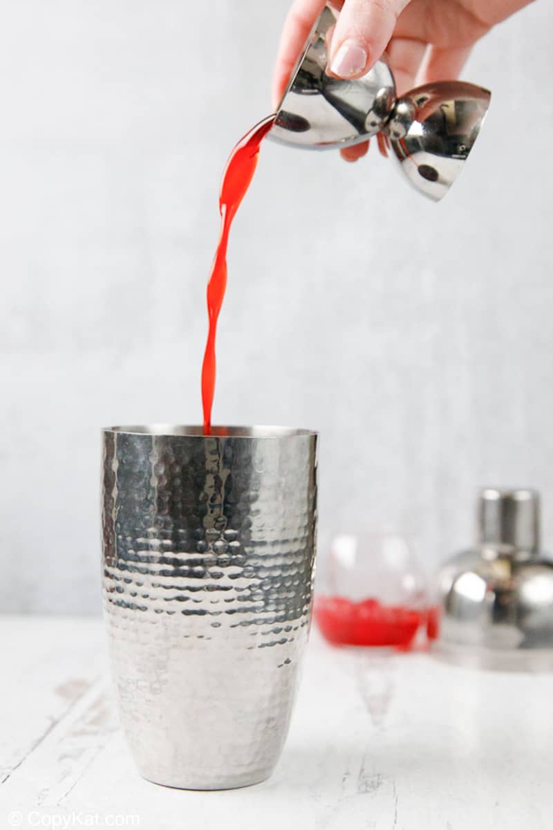 pouring cherry syrup into a cocktail shaker