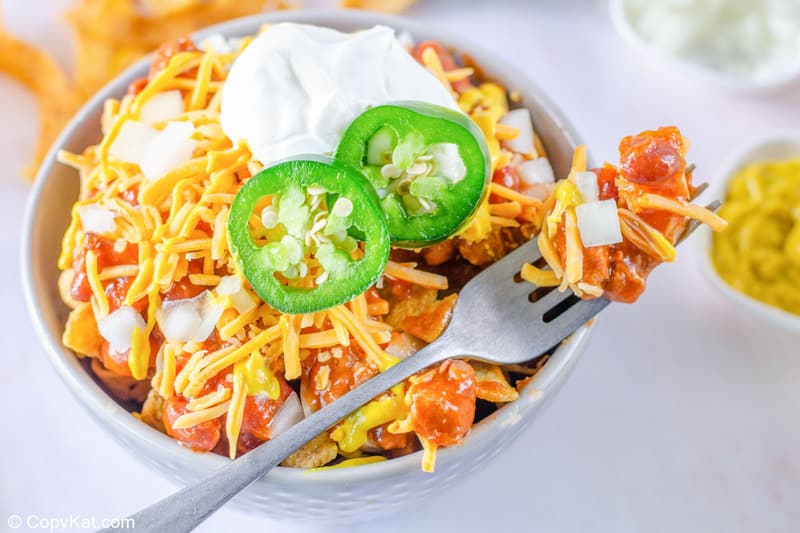 Frito pie on a fork sitting on the side of a bowl of the pie