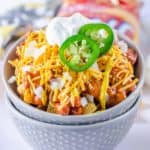 a bowl of Frito Pie topped with onions, sour cream, and jalapeno slices