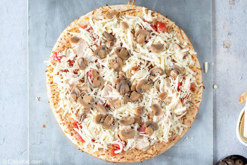 pizza crust topped with tomatoes, chicken, cheese, and mushrooms