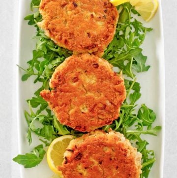 three salmon patties, lemon slices, and arugula on a platter