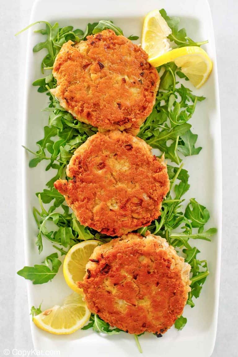 three salmon patties, lemon slices, and arugula on a platter