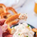 hand holding a pretzel with beer cheese dip on it