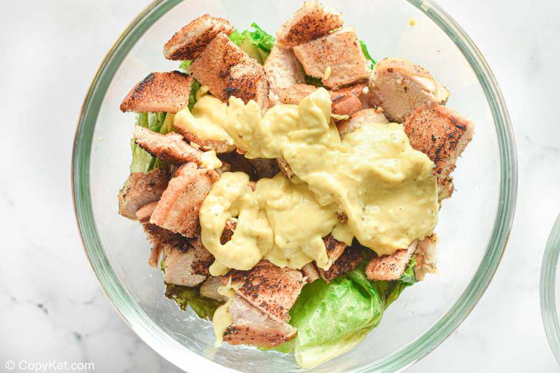 romaine lettuce, chicken, croutons, and Caesar dressing in a bowl