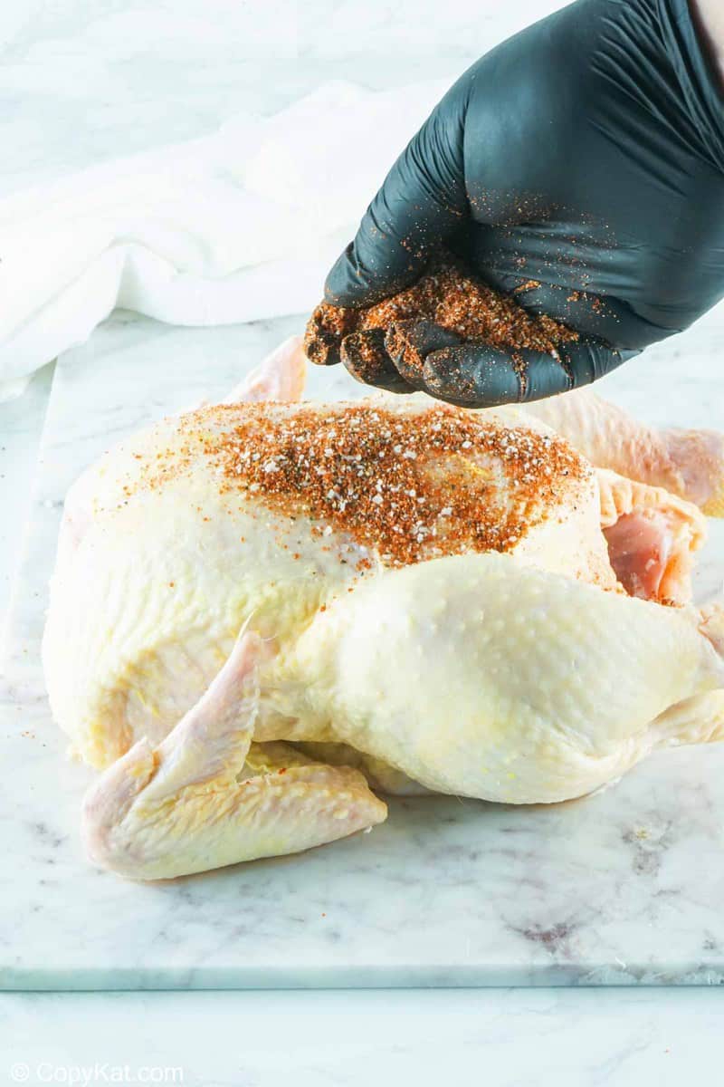 sprinkling seasoning on a whole chicken