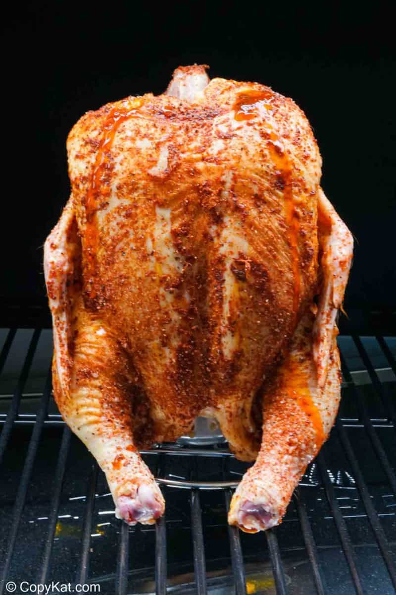 seasoned chicken on a beer can chicken holder in a smoker