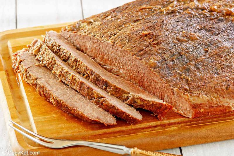 oven baked brisket, slices, and a meat fork on a wood cutting board