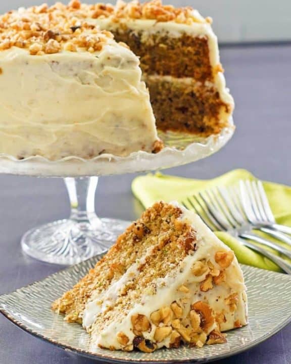zucchini cake with cream cheese frosting on a cake stand and a slice on a plate