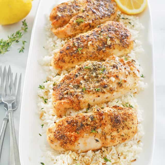 baked lemon pepper chicken with garlic over rice on a platter