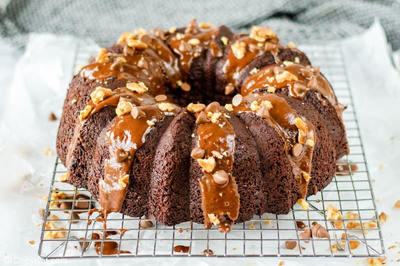 chocolate bundt cake with chocolate glaze, chocolate chips, and nuts on top.