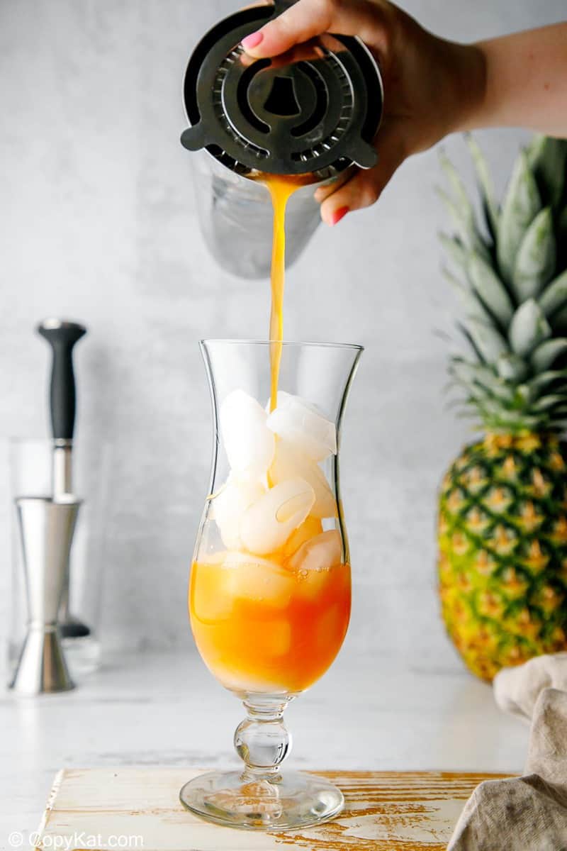 pouring rum punch into a glass filled with ice