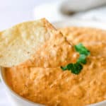 taco dip on a tortilla chip over a bowl of the dip.