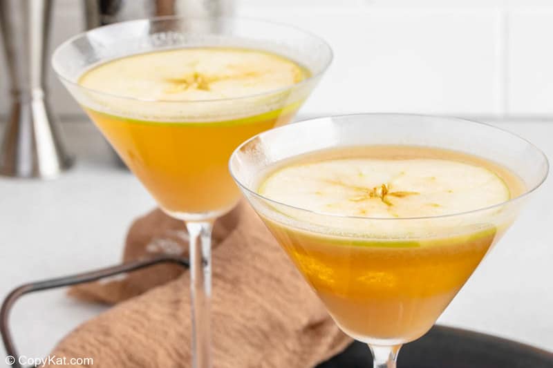 two caramel apple martini cocktails garnished with apple slice