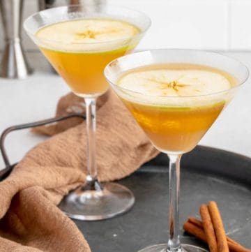 two caramel apple martinis and cinnamon sticks on a tray