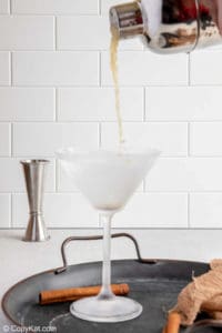 pouring a caramel apple martini from a cocktail shaker into a martini glass