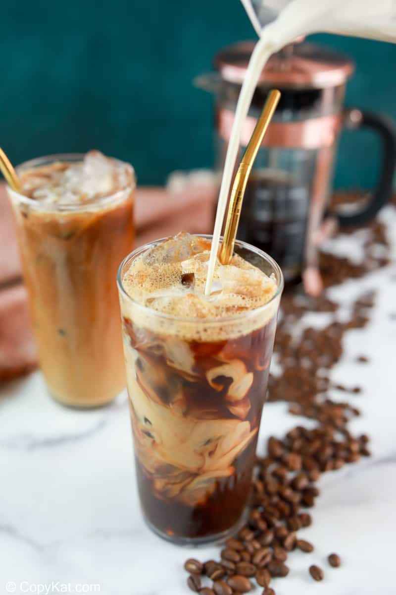 pouring vanilla sweet cream into a glass with cold brew coffee and ice.