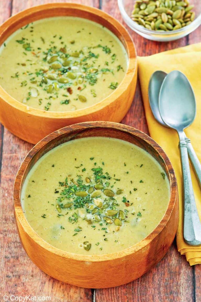 two bowls of acorn squash soup, a bowl of pumpkin seeds, and two spoons.
