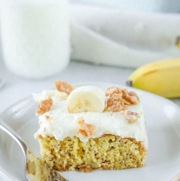 banana cake slice and a fork on a plate and a glass of milk.