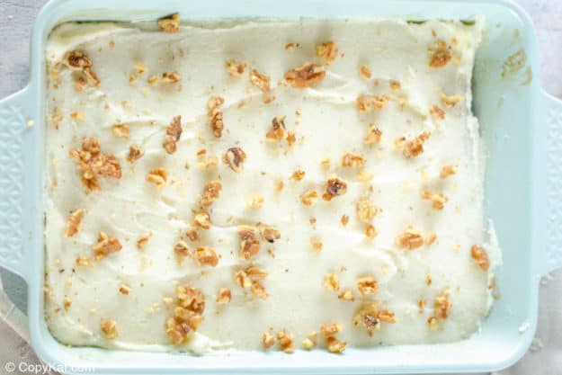 banana cake topped with cream cheese frosting and nuts in a baking dish.