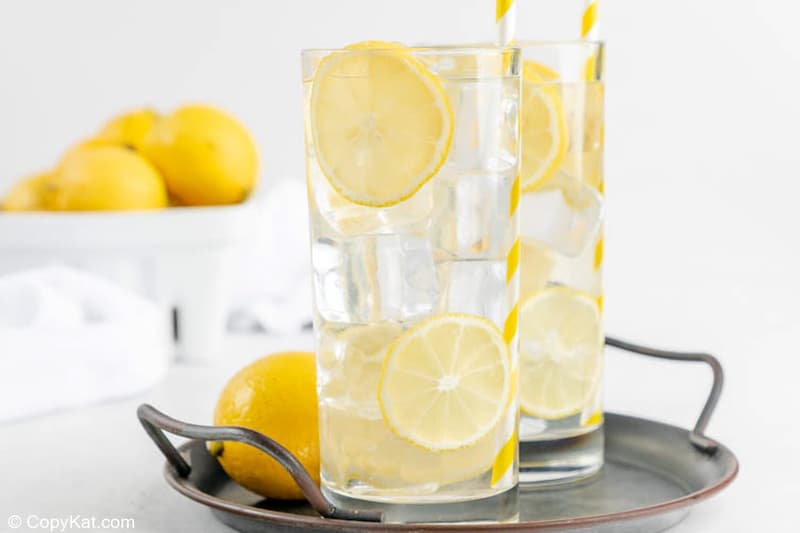 two glasses of homemade lemonade on a tray and a basket of lemons.