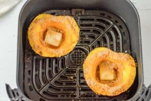 acorn squash with butter and brown sugar in an air fryer basket.