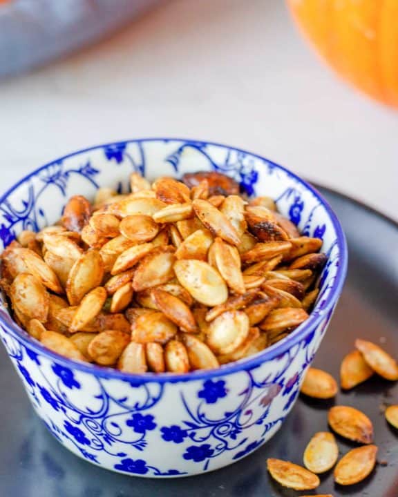 air fryer pumpkin seeds in a blue bowl on top of a black plate.