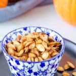 air fryer pumpkin seeds in a small blue bowl on a black plate.
